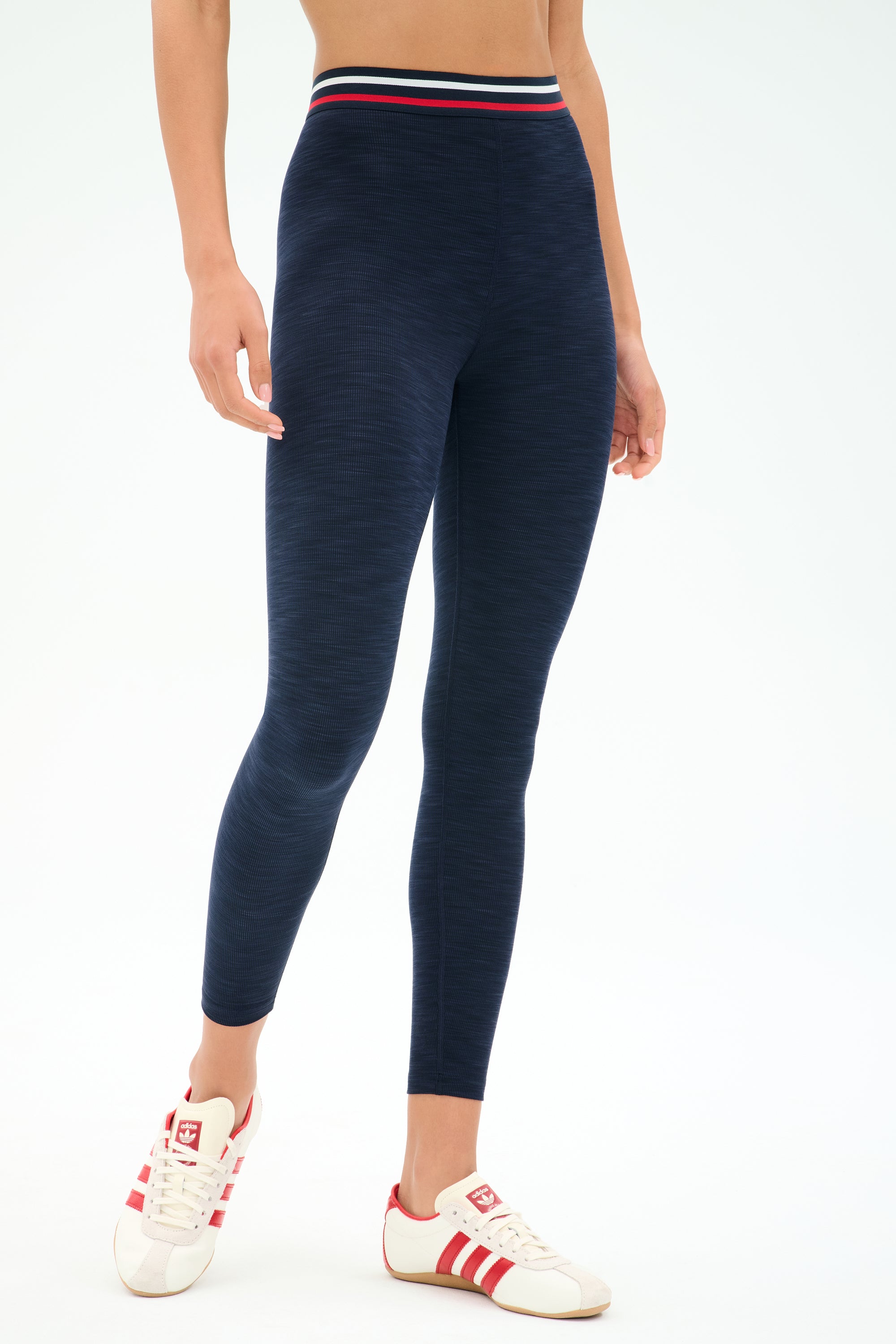 Person wearing SPLITS59 Bailey High Waist Active Rib 7/8 leggings in Heather Indigo, featuring a striped waistband, paired with white sneakers with red stripes—ideal gym wear.