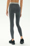 A person faces away, wearing SPLITS59 Bailey Active Rib High Waist 7/8 leggings in Heather Grey with a white-striped waistband and black sneakers, set against a plain background—ideal for gym workouts.