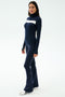 A woman wears the SPLITS59 Lennon Rib Turtleneck in Indigo/White with matching navy flared pants and white sneakers, standing against a plain background.