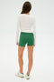 A person wearing a SPLITS59 Louise Rib Long Sleeve in white, along with green shorts and white sneakers, stands facing away against a plain background.