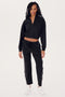 A person is dressed in the SPLITS59 Lucy Rigor Pant W/Piping in black with white stripes and white sneakers, standing on a plain white background. The relaxed-fit jogger ensures all-day comfort, ideal for any activity.