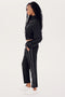 Wearing the SPLITS59 Lucy Rigor Pant W/Piping in black with white side stripes and white sneakers, a person in profile against a plain background exudes all-day comfort with this relaxed fit jogger design that ensures ease of movement and style.