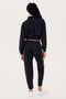 Someone wearing the SPLITS59 Lucy Rigor Pant W/Piping in black and white sneakers stands against a plain background, with their back to the camera, exuding all-day comfort.