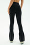 A person stands with their back to the camera against a plain white background, wearing SPLITS59 Raquel High Waist Flared Legging in Black/Creme and white sneakers.