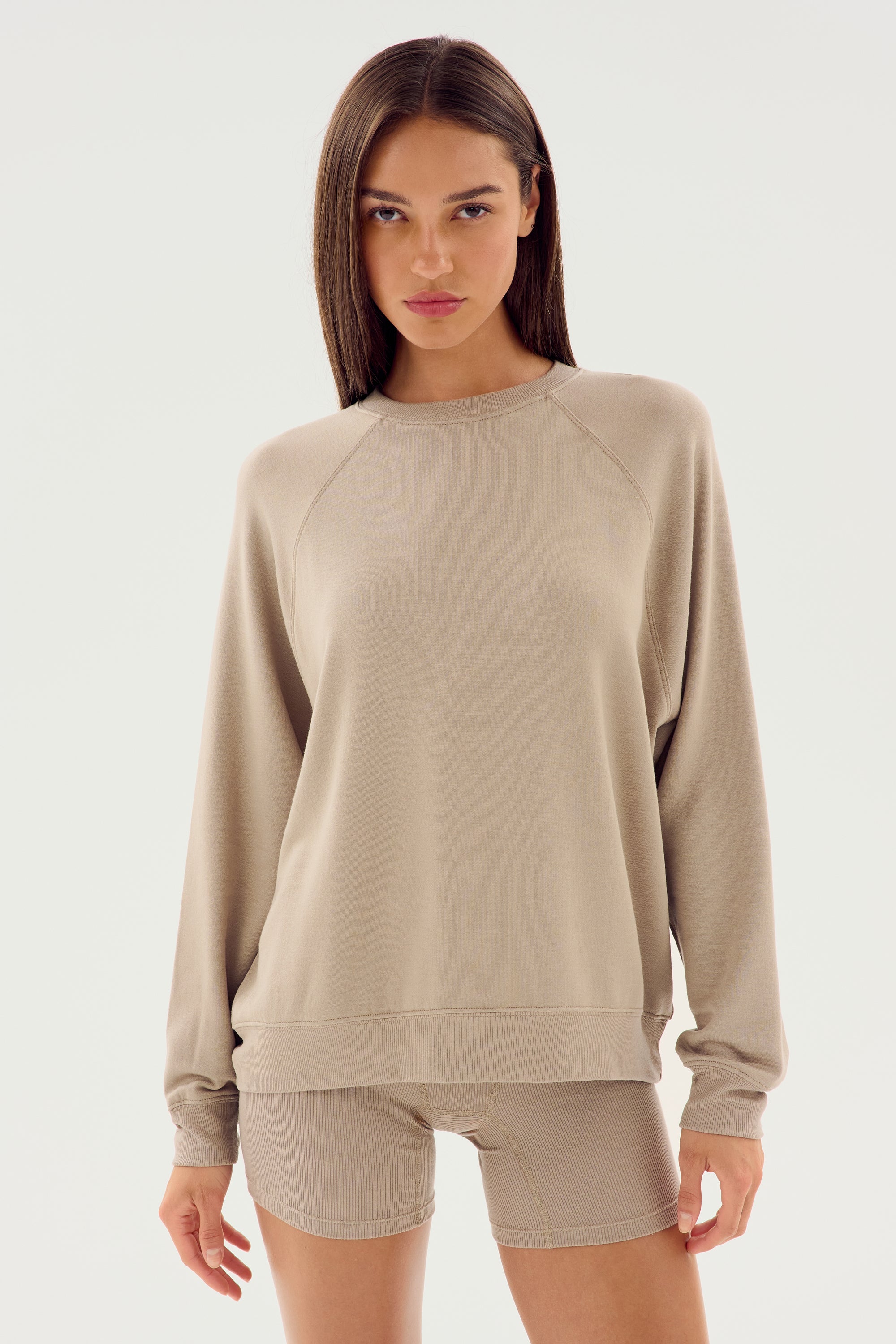 A person with long straight hair, dressed in an Andie Fleece Sweatshirt - Latte by SPLITS59 and matching shorts made from stretch modal fabric, stands against a plain white background.