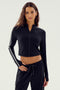 Woman wearing the SPLITS59 Leo Airweight Jacket Crop in black with white sleeve stripes, paired with matching black spandex pants, standing against a plain background.