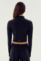 A person with long hair is seen from the back wearing a SPLITS59 Leo Airweight Jacket Crop in Black/White and black spandex pants against a plain background.