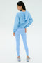 A person stands facing away, wearing the SPLITS59 Megan Woven Nylon Jacket in Skylight against a plain light background.