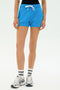 Model wearing the SPLITS59 Reena Sweatshort in Riviera, paired with white athletic socks and white sneakers, standing against a plain white background.