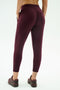 Back view of a person wearing SPLITS59 Reena Fleece 7/8 Sweatpant in Dark Cherry, paired with dark sneakers, standing against a plain light background.