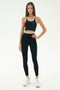 A woman stands against a plain background wearing SPLITS59's Dual High Waist Airweight 7/8 leggings in Black/White, paired with a black sports bra with white trim and white athletic shoes.