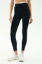 A person models the SPLITS59 Dual High Waist Airweight 7/8 leggings in black/white, paired with white sneakers, standing against a plain light background.