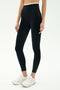 Model wears SPLITS59 Dual High Waist Airweight 7/8 leggings in black/white, paired with white athletic shoes, posed against a plain light background.