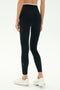 A person is shown from the back wearing SPLITS59’s Dual High Waist Airweight 7/8 leggings in Black/White with white sneakers, standing against a plain white background.