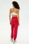 A person faces away, wearing a white sports bra and SPLITS59 Andie Oversized Fleece Sweatpant in Pirate Red, perfect for cool weather workouts or warm-ups, with white sneakers against a plain light background.