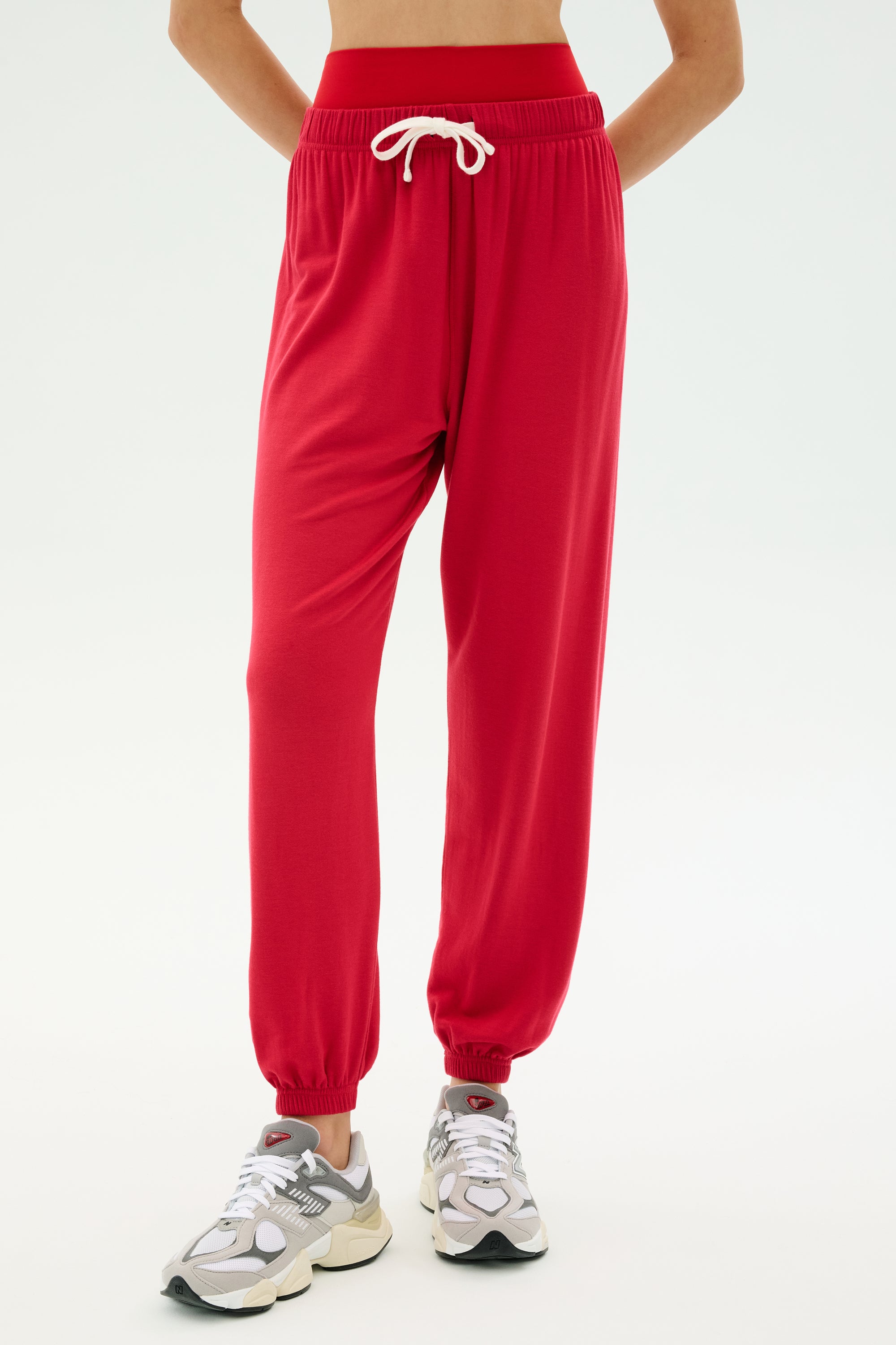 Someone wearing the SPLITS59 Andie Oversized Fleece Sweatpant in Pirate Red with a white drawstring and gray running shoes, posed against a light backdrop—ideal for cozy warm-ups or cool weather workouts.