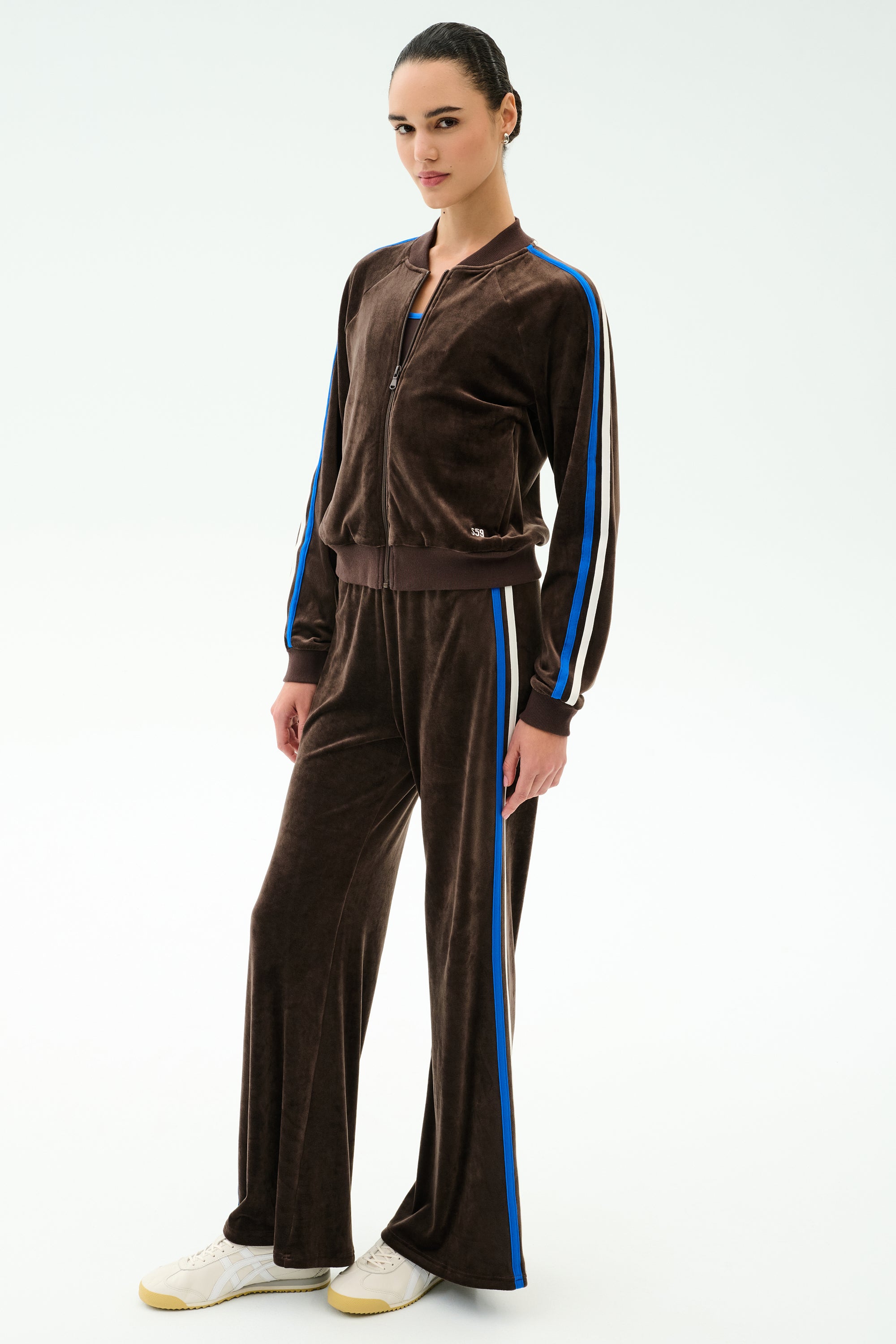 A person wearing the SPLITS59 Heritage Velour Bomber in Dark Chocolate/Classic Blue with matching striped pants warms up against a plain white background.