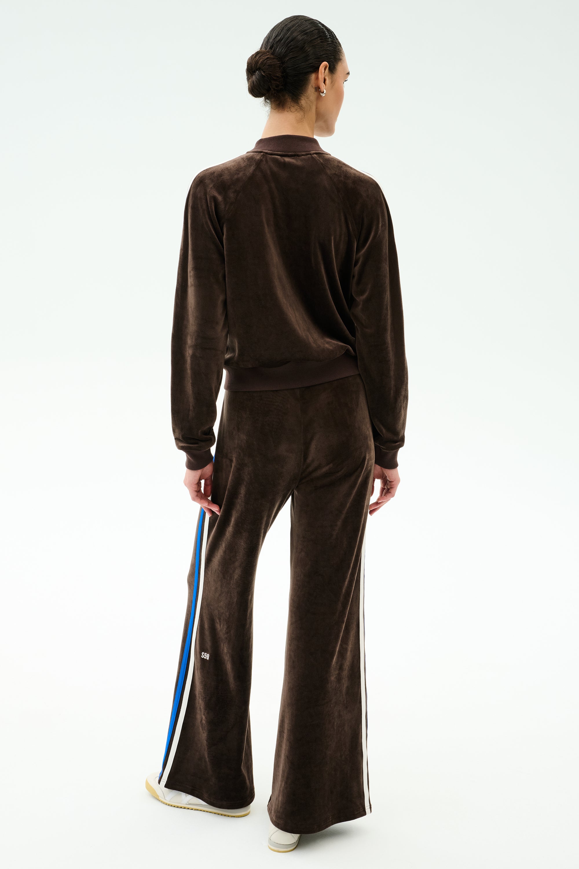 Person faces away from the camera wearing SPLITS59’s Heritage Velour Pant in Dark Chocolate/Classic Blue, a flared wide-leg style with side stripes, set against a plain white background.
