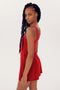 Woman with long braids in a red sleeveless Martina Rigor Dress w/Piping - Pirate Red, made by SPLITS59, standing against a white background, looking over her shoulder.