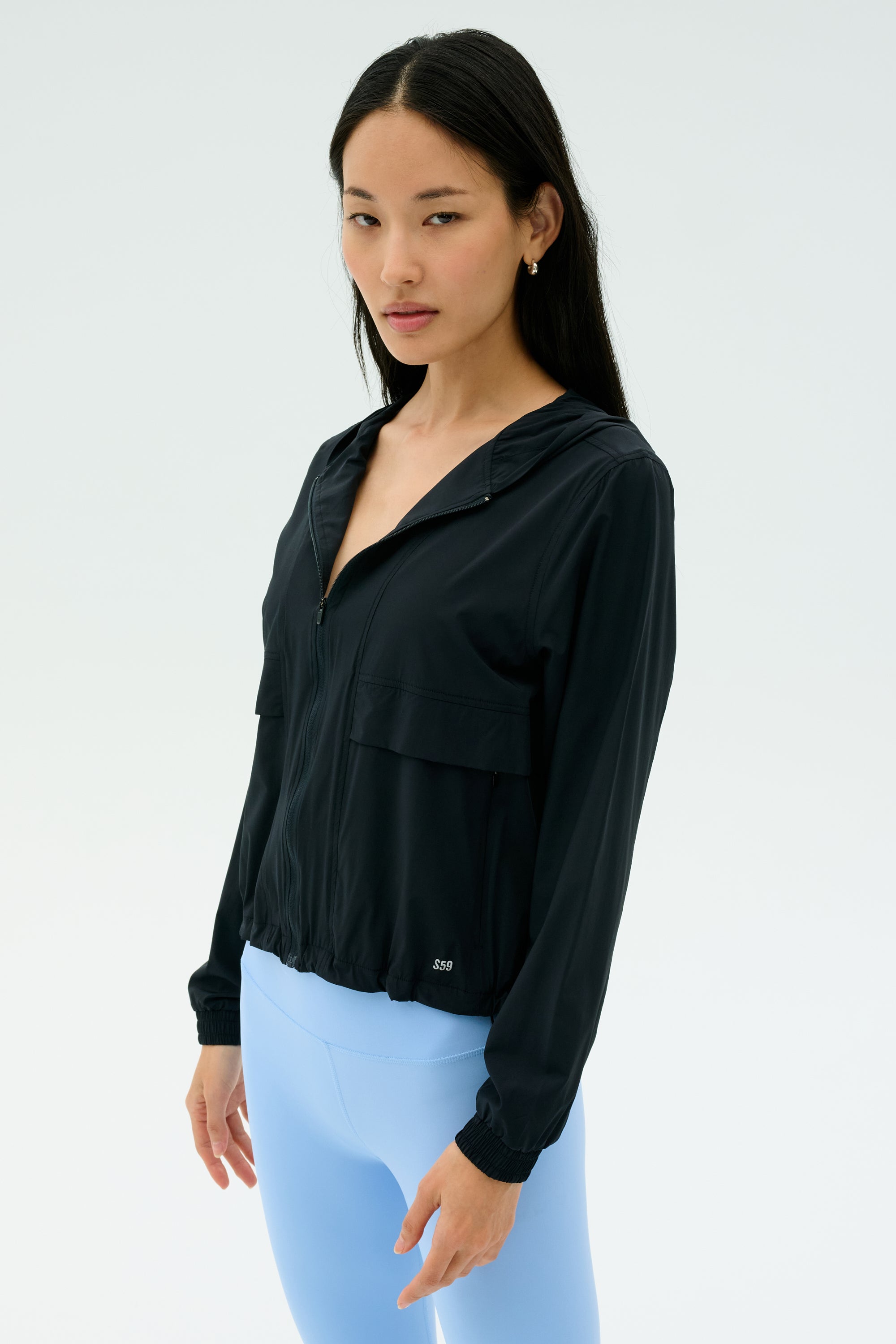 A woman wears the SPLITS59 Megan Woven Nylon Jacket in black, standing against a plain, light background.
