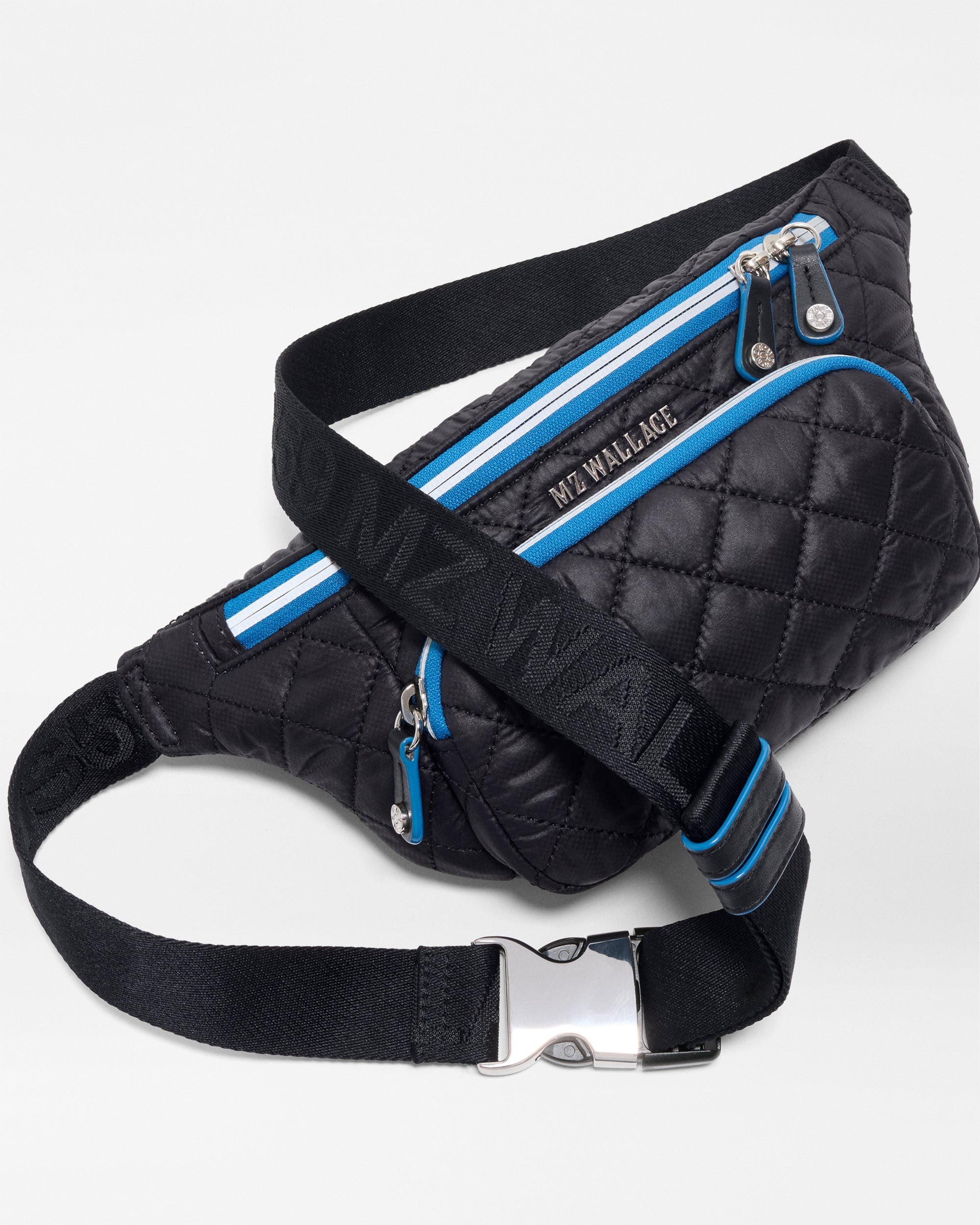 The SPLITS59 MZW x Splits59 Small Metro Sling features a black quilted design, blue zipper accents, an adjustable black strap with blue stripes, and silver hardware, shown against a white background.
