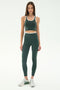 A woman stands facing forward wearing the SPLITS59 Amber Airweight Bralette in Military/White and matching leggings, both made from Airweight performance fabric, with white athletic shoes, against a plain light background.