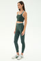 A woman stands against a plain background wearing the SPLITS59 Dual High Waist Airweight 7/8 leggings in Military/White with a matching sports bra and white sneakers.