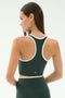 A woman stands with her back to the camera, wearing the SPLITS59 Amber Airweight Bralette in Military/White—crafted from performance fabric with white trim—perfect for hot yoga.
