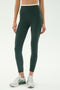 A person wears SPLITS59 Dual High Waist Airweight 7/8 leggings in Military/White with white athletic shoes, standing on a plain light background.