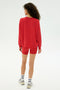 A person with curly hair faces away, wearing the SPLITS59 Andie Fleece Sweatshirt in Pirate Red, matching red shorts, white socks, and white sneakers against a plain light background.