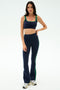 A woman stands in the SPLITS59 Raquel High Waist Supplex Flare in Indigo/Grass—navy and green activewear with 4-way stretch—paired with a crop top and white sneakers, ideal for any workout, against a plain white background.