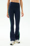 A person wears SPLITS59 Raquel High Waist Supplex Flare leggings in Indigo/Grass with white sneakers, standing against a plain light background. These leggings offer 4-way stretch for ultimate comfort—ideal for your next workout session.