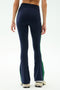 A person stands with their back shown, wearing SPLITS59 Raquel High Waist Supplex Flare leggings in Indigo/Grass and white sneakers. The 4-way stretch fabric makes them perfect for workouts. Plain background.