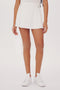 A close-up of a person wearing a SPLITS59 Venus High Waist Rigor Skort w/Piping - White and white sneakers, focusing on the lower torso down to the feet.