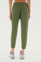 A person is standing facing away, wearing the SPLITS59 Reena Fleece 7/8 Sweatpant in olive and gray sneakers. Made from a feminine drape stretch modal fabric, these sweatpants feature a back pocket on the right side.