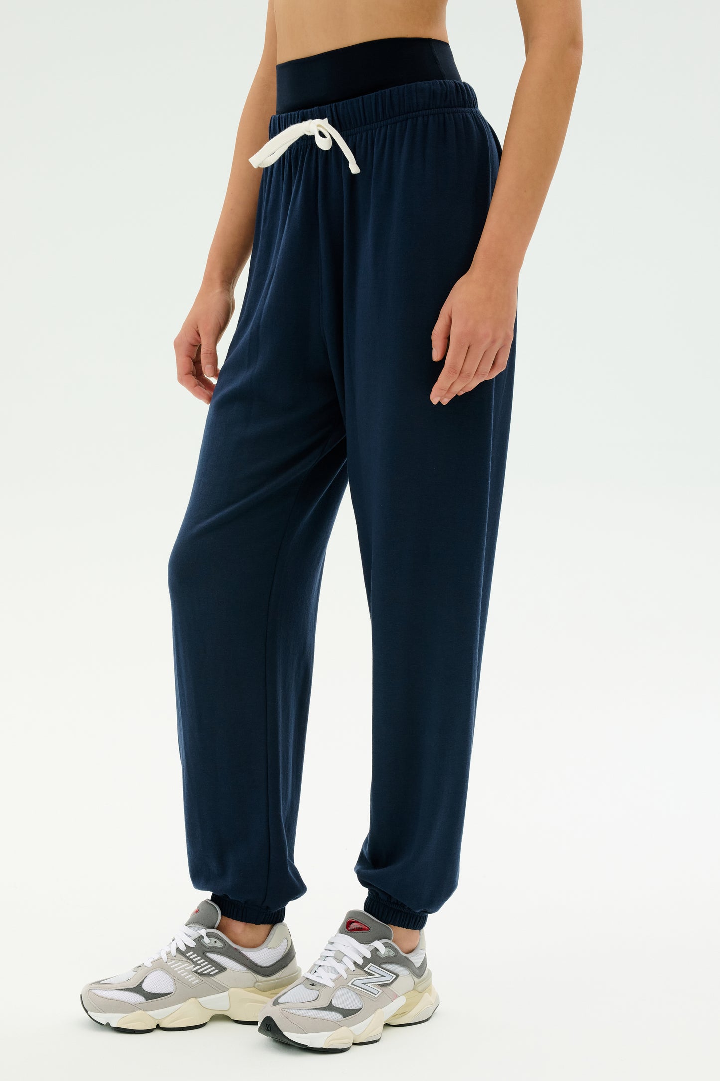 Model wears the SPLITS59 Andie Oversized Fleece Sweatpant in Indigo, featuring a white drawstring and paired with grey sneakers—ideal for cool weather workouts—standing against a plain white background.