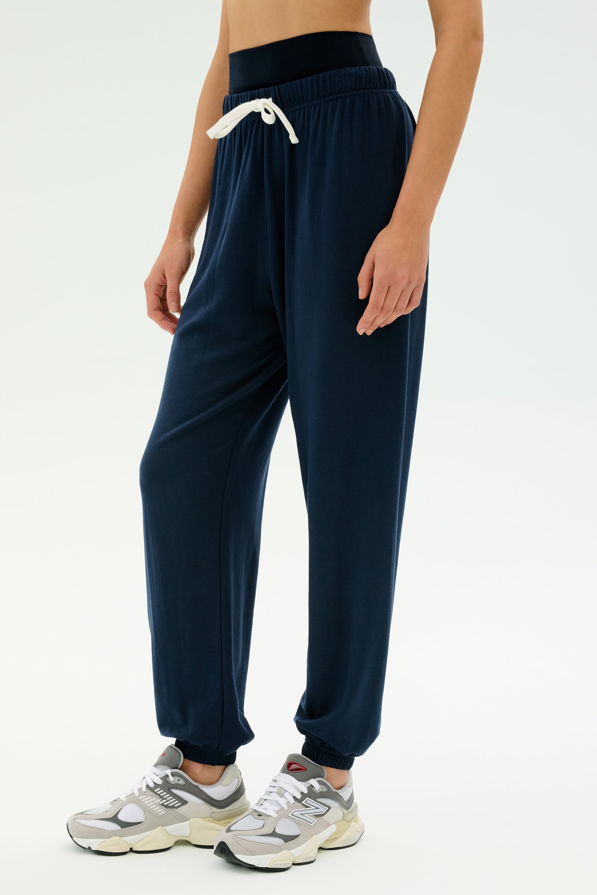 Model wears the SPLITS59 Andie Oversized Fleece Sweatpant in Indigo, featuring a white drawstring and paired with grey sneakers—ideal for cool weather workouts—standing against a plain white background.