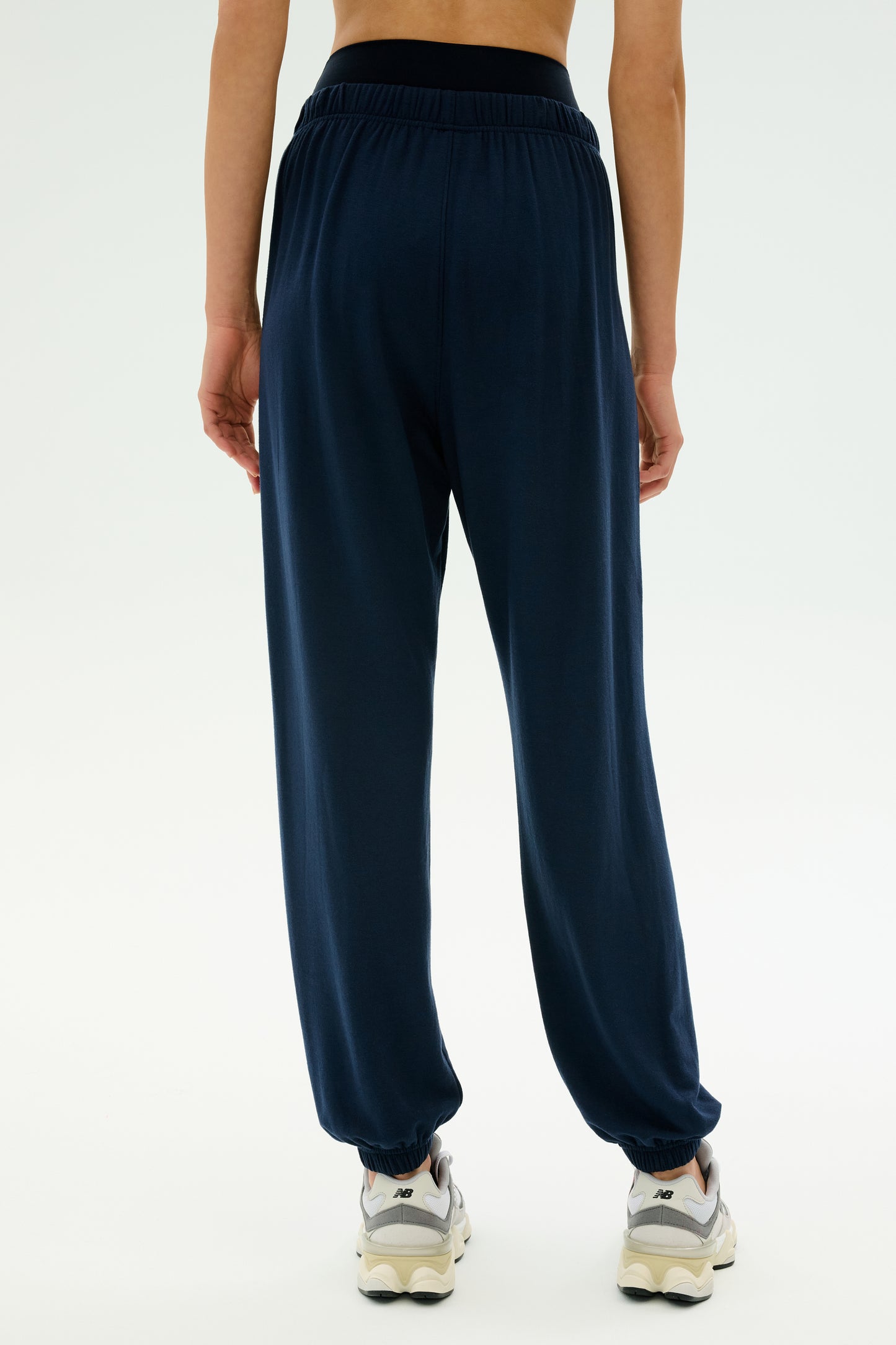 Person wearing SPLITS59 Andie Oversized Fleece Sweatpant in Indigo and white sneakers, shown from the back against a plain light background—perfect for cool weather workouts. MADE IN LOS ANGELES.
