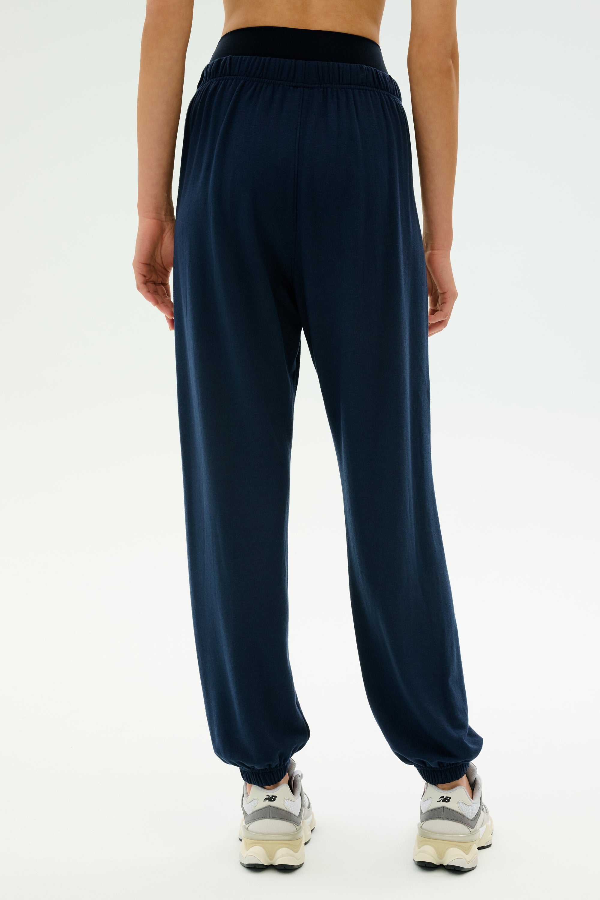 Person wearing SPLITS59 Andie Oversized Fleece Sweatpant in Indigo and white sneakers, shown from the back against a plain light background—perfect for cool weather workouts. MADE IN LOS ANGELES.