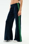 A person models the SPLITS59 Heritage Velour Pant in Indigo/Grass, featuring green side stripes, paired with white sneakers against a plain white background.
