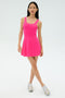 A person stands against a plain light background wearing the SPLITS59 Martina Rigor Dress in Berry and silver athletic shoes.