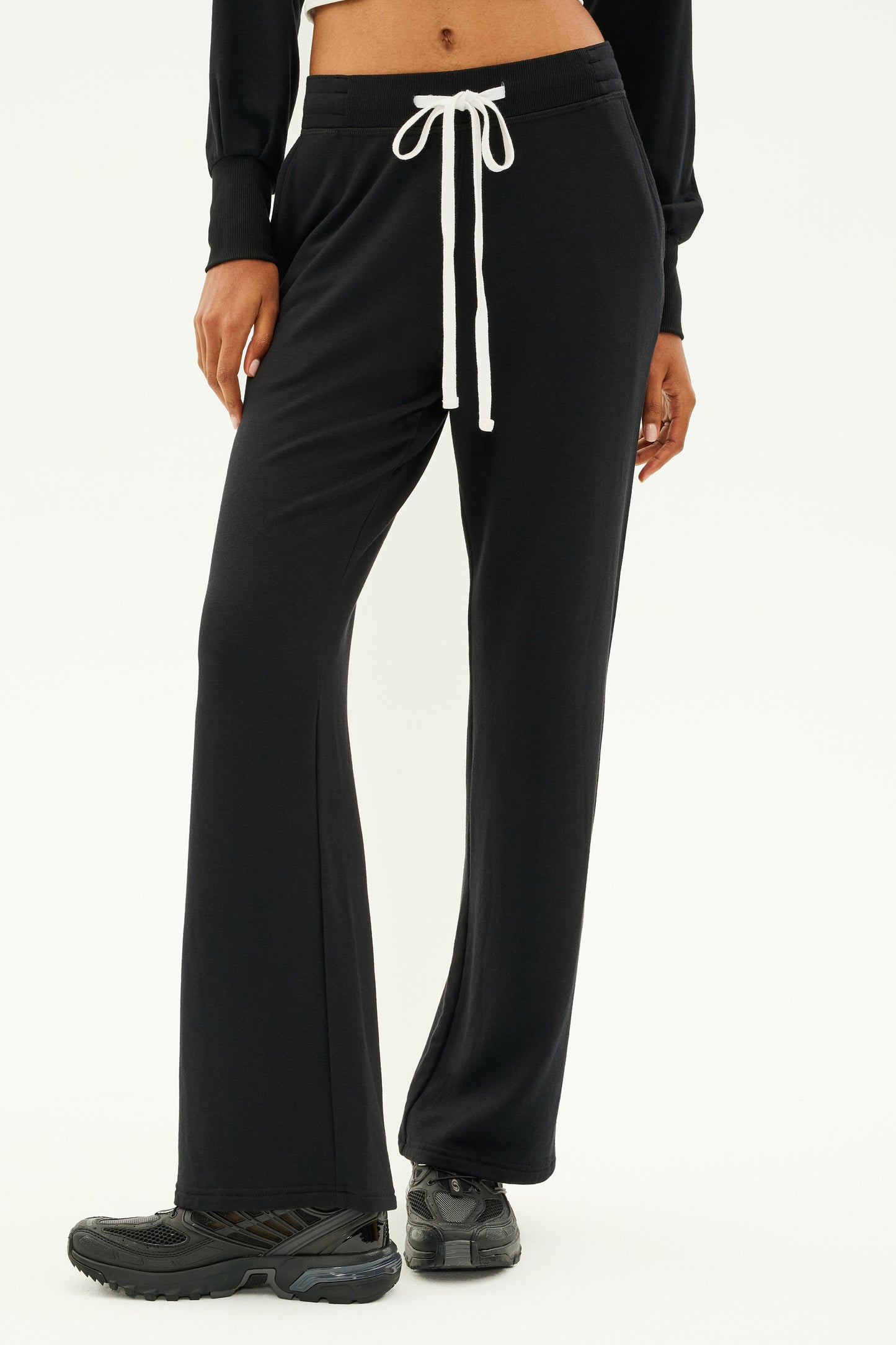 A person wearing the SPLITS59 Raven Fleece Full Length Sweatpant in black, featuring a white drawstring and made from ultra-luxe fleece, paired with black sneakers, is standing on a white background. MADE IN LOS ANGELES.