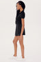 Young woman with braided hair standing sideways wearing a SPLITS59 Talia Rib Polo in Black, black skirt, and white sneakers, ready for gym workouts.