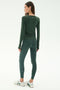 A woman faces away, wearing the SPLITS59 Airweight Lite LS Waist Length top in Military with matching leggings and white sneakers, set against a plain light background.
