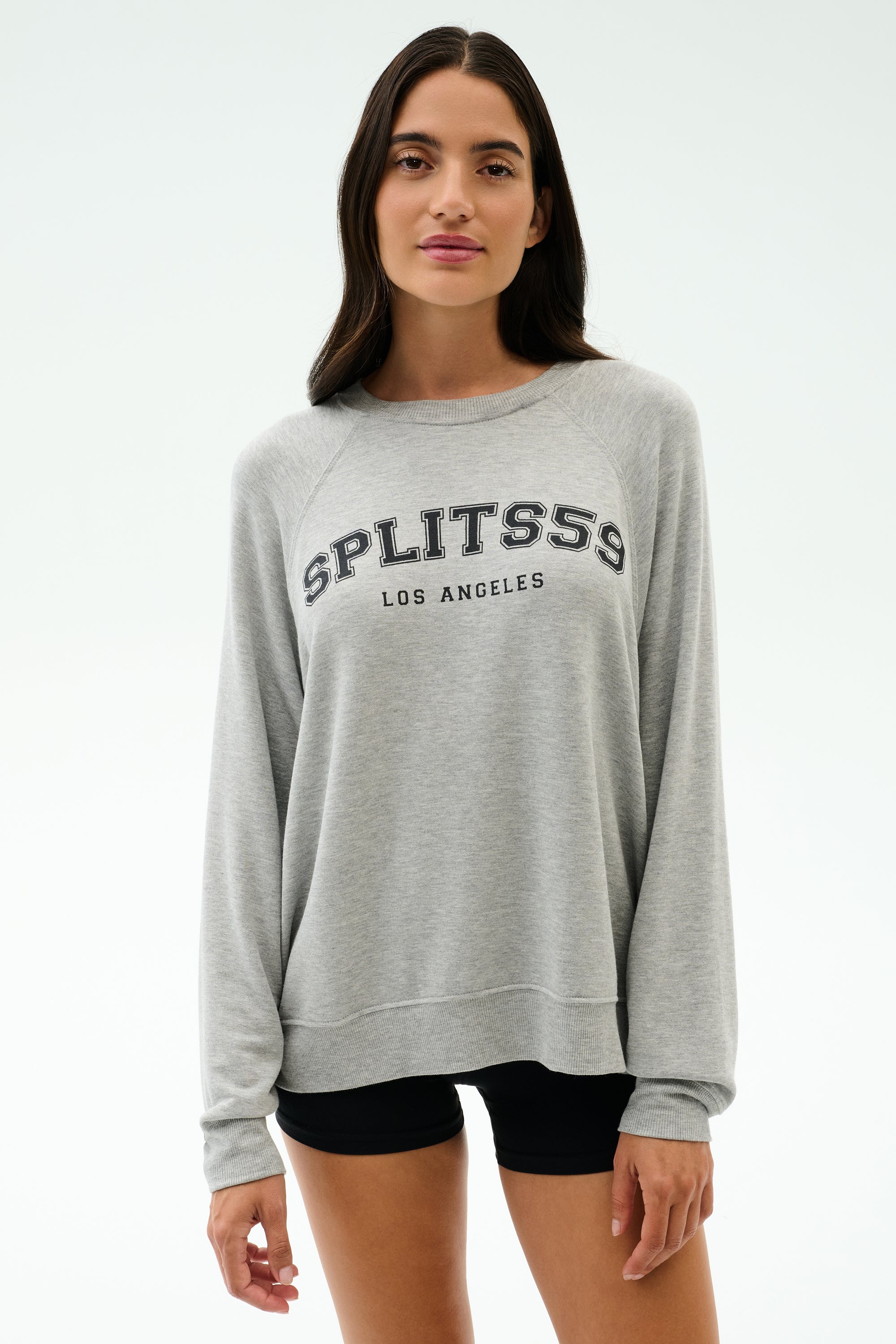 A woman faces the camera wearing the SPLITS59 Andie Oversized Fleece Varsity Graphic Sweatshirt in Heather Grey with "SPLITS59 LOS ANGELES" on the front, paired with black shorts.