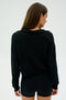 A long-haired individual is facing away, wearing SPLITS59's Joan Fleece Polo Sweatshirt in black along with black shorts.