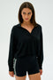 A person in a black SPLITS59 Joan Fleece Polo Sweatshirt and black shorts with green and white stripes stands against a plain background.