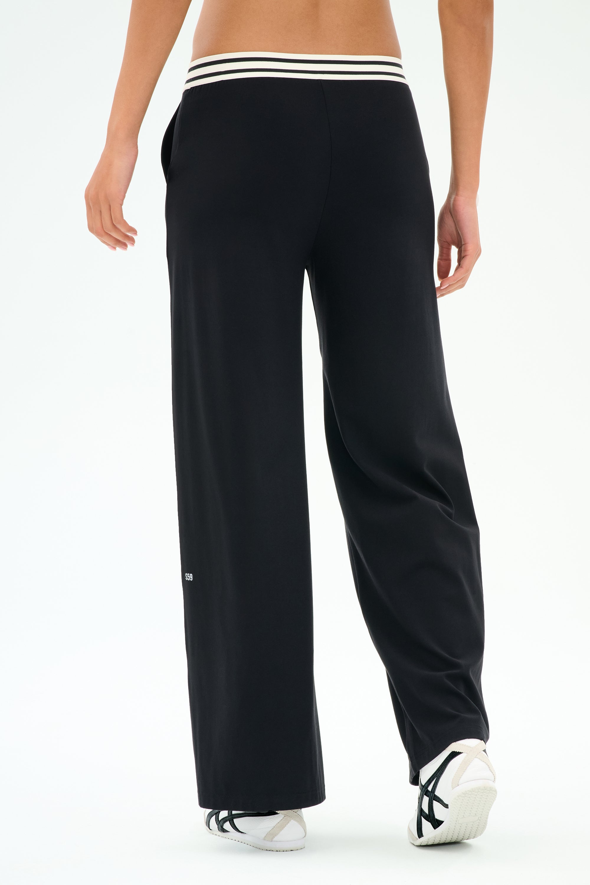 Person wearing SPLITS59 Michele Airweight Trouser in black, featuring a white striped waistband, paired with white sneakers and shown from the back.