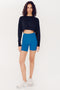 A woman in a SPLITS59 Noah Fleece Crop Sweatshirt - Black and blue bike shorts standing against a white background.