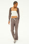 A person wearing a white tube top and gray cardigan, styled with SPLITS59's Raven Fleece Full Length Sweatpant in Lentil, stands with hands in pockets, looking down.